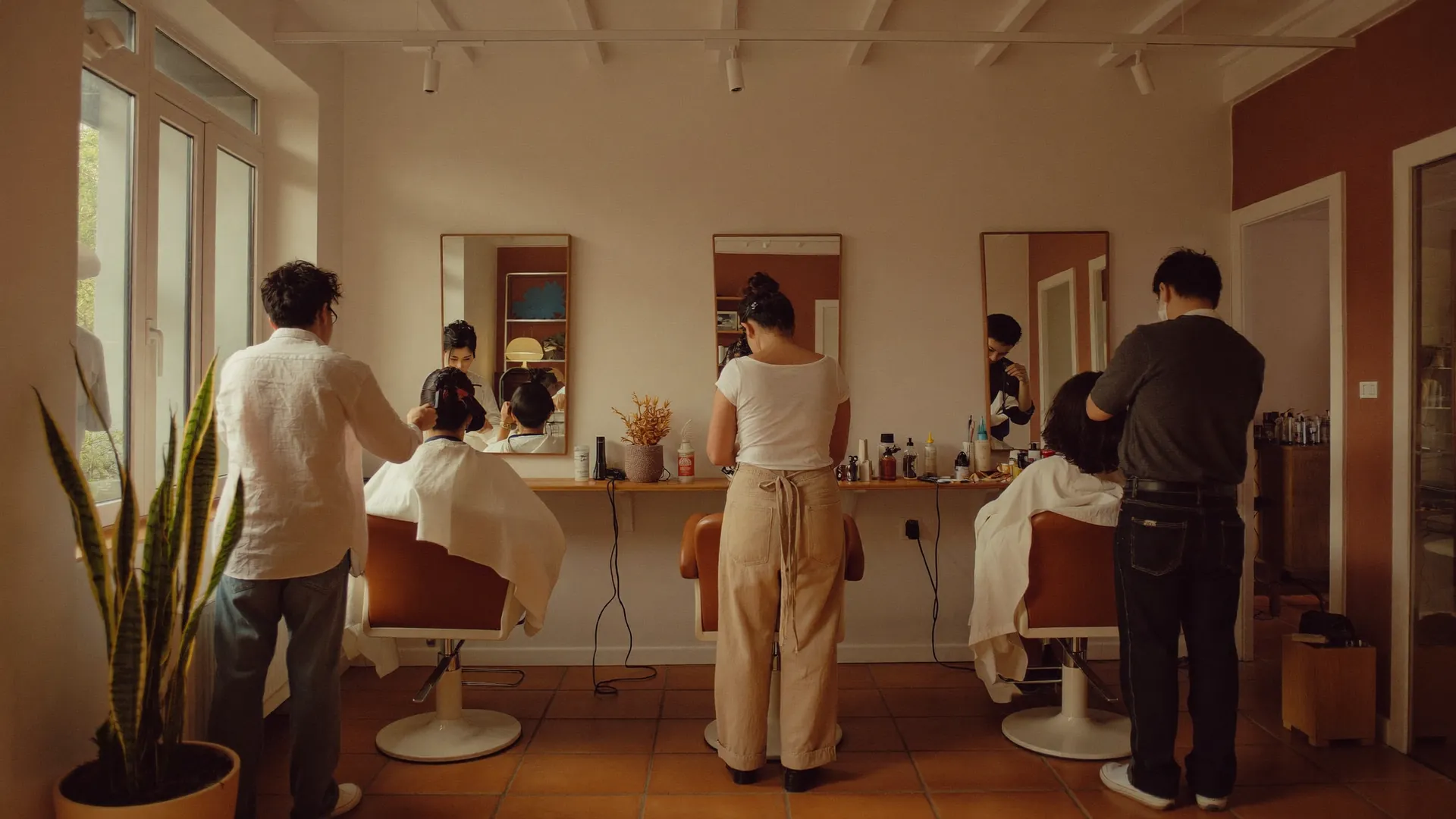 Drei Friseure arbeiten mit Kundinnen an Spiegelplätzen in einem warmen Salon